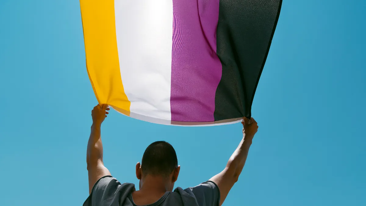 A person holding a nonbinary pride flag is seen from behind.