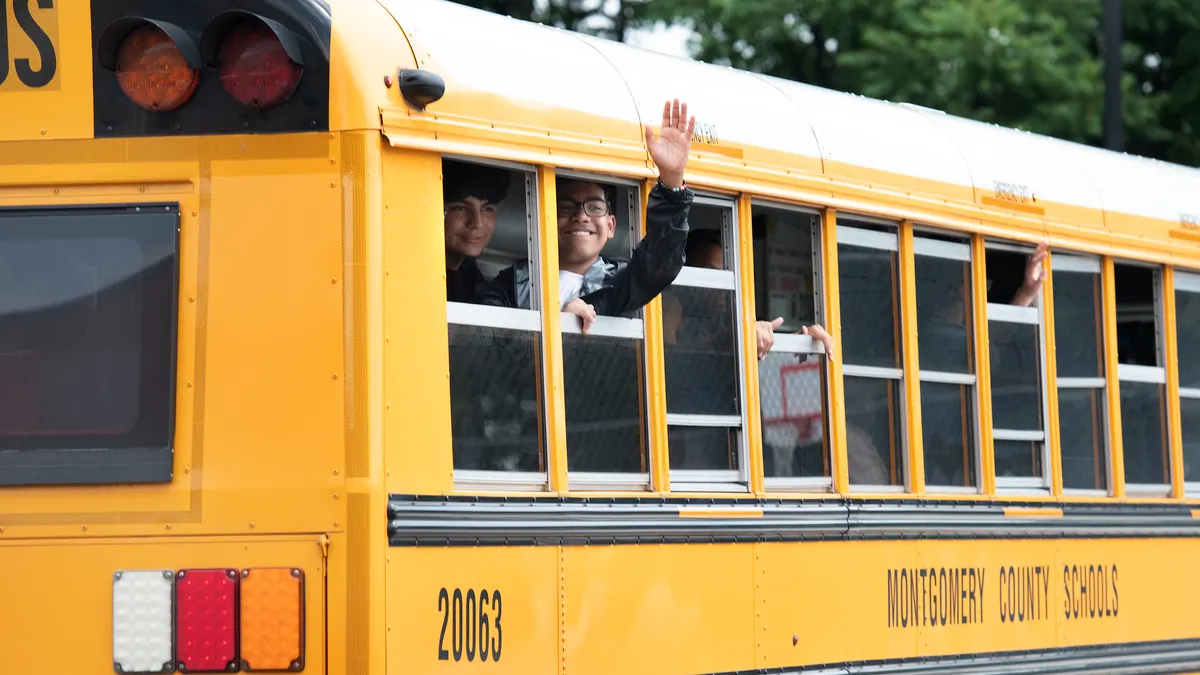 A waving student leans out of a school bus