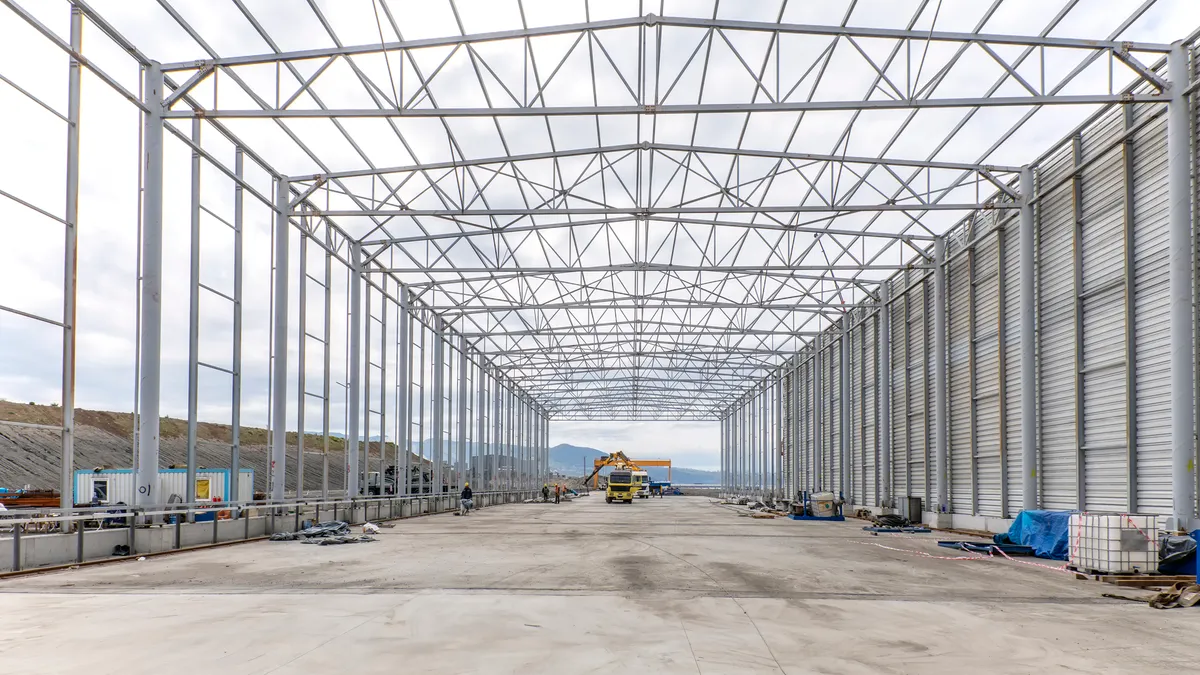 A skeleton steel frame of an industrial construction project rises against the sky.