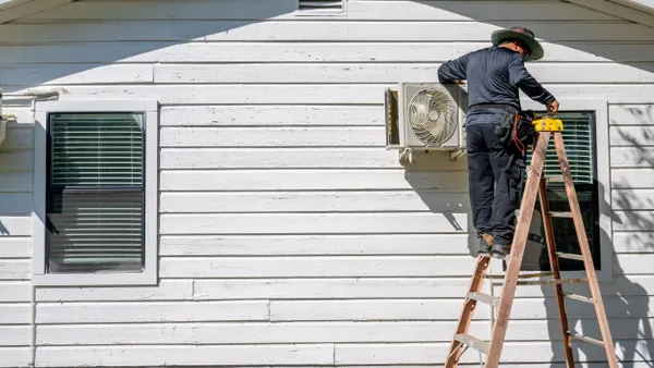 An individual stands on a ladder, working on an air conditioning unit.