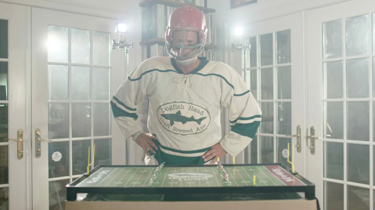 A man in a Dogfish Head Jersey and red helmet play a Game of Electric Football.