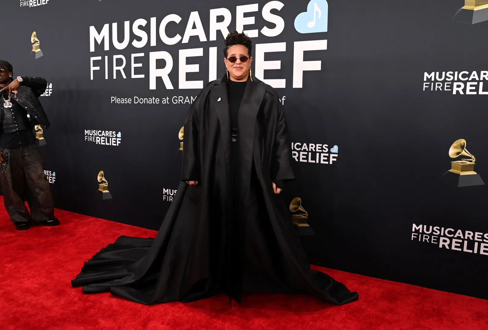 A person in an voluminous black outfit stands on the red carpet.