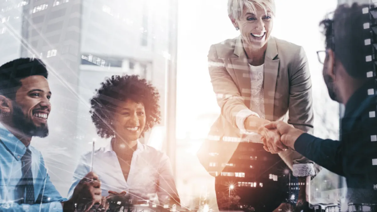 Four business workers in profressional clothing, with two business people shaking hands and smiling.