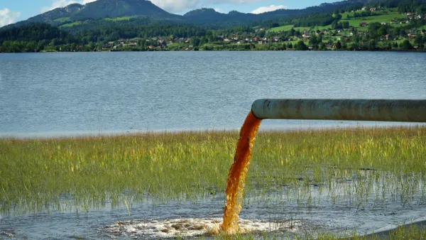 A pipe containing dirty water is draining into a lake. A town lies on the banks in the background.