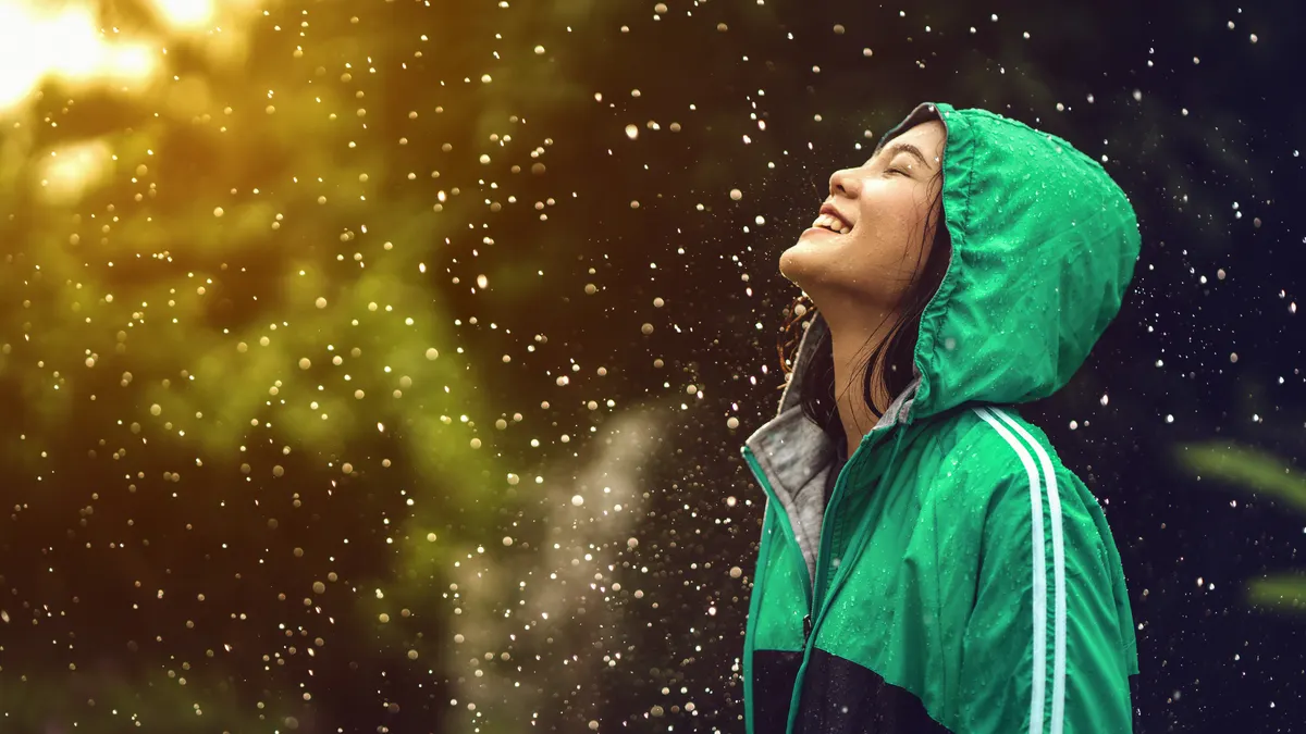 Woman wearing a rain coat standing in the rain while smiling.