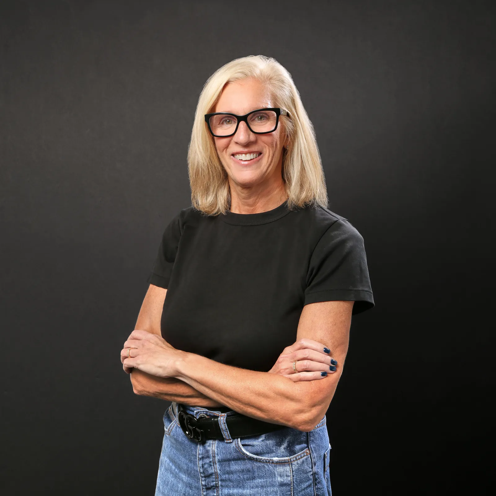 A headshot portrait of Tommy John CEO Cheryl Abel-Hodges, who has light hair, dark rimmed eyeglasses and a black shirt.