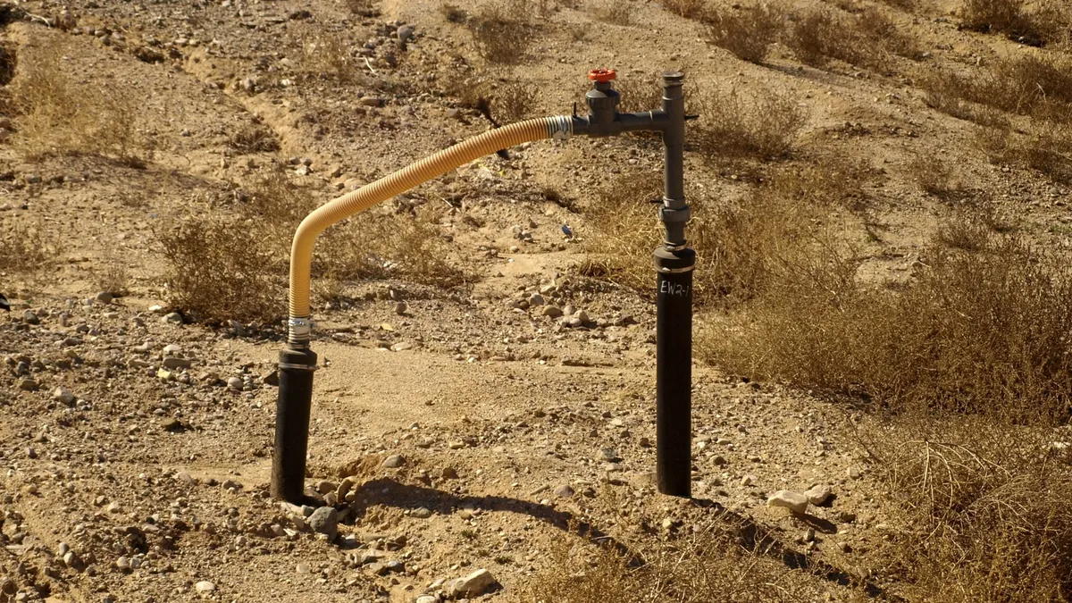 Two small pipes connected by a flexible tube stick out of rocky soil.