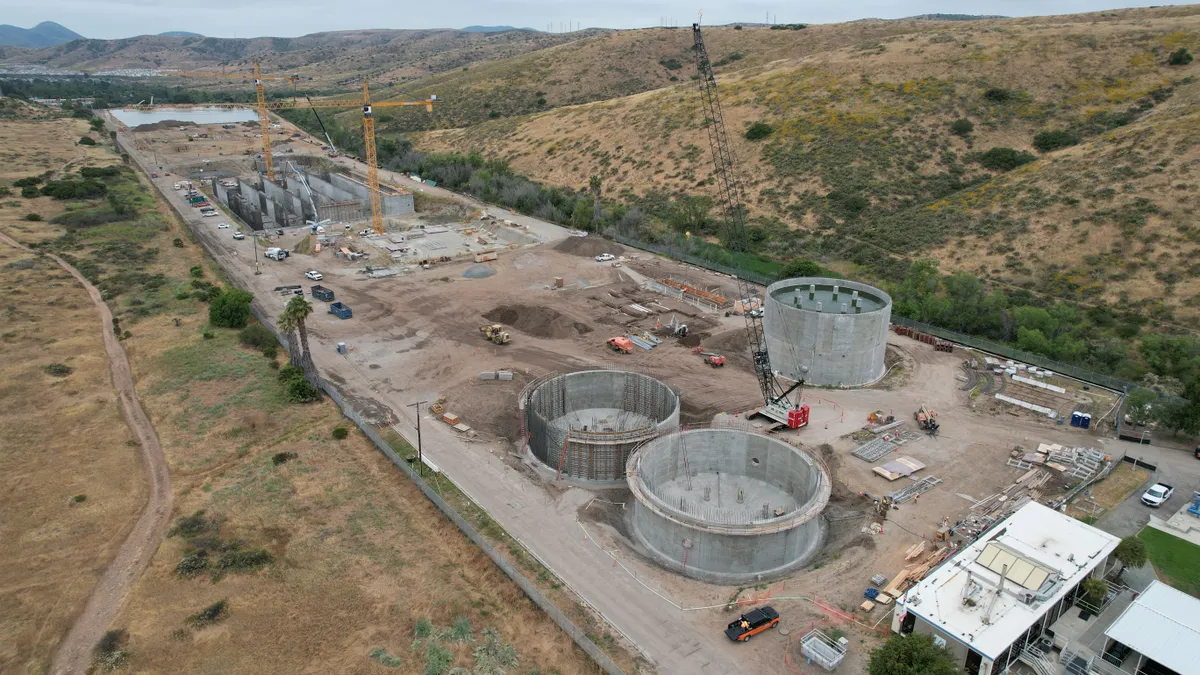 An industrial site in the early stages of construction, with cranes and the base of cylindrical concrete towers visible.