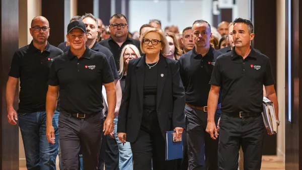 Over a dozen Unifor union members walk down a hall, wearing matching black shirts, with leaders at the front.