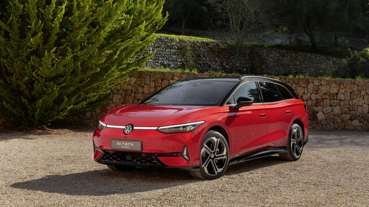 A red electric Volkswagen ID.7 Tourer model parked on a gravel surface with a stone wall and greenery in the background.