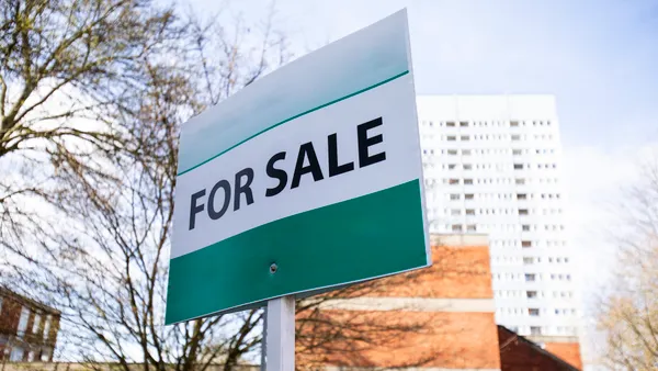 For sale sign with apartment building in the background