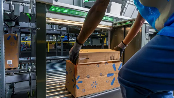 A Walmart worker lifts a box off a conveyer belt.