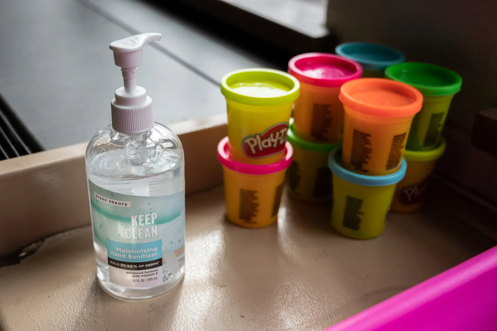 A pump bottle of hand sanitizer sits on a desk next to stacked cans of colorful Play-Doh.