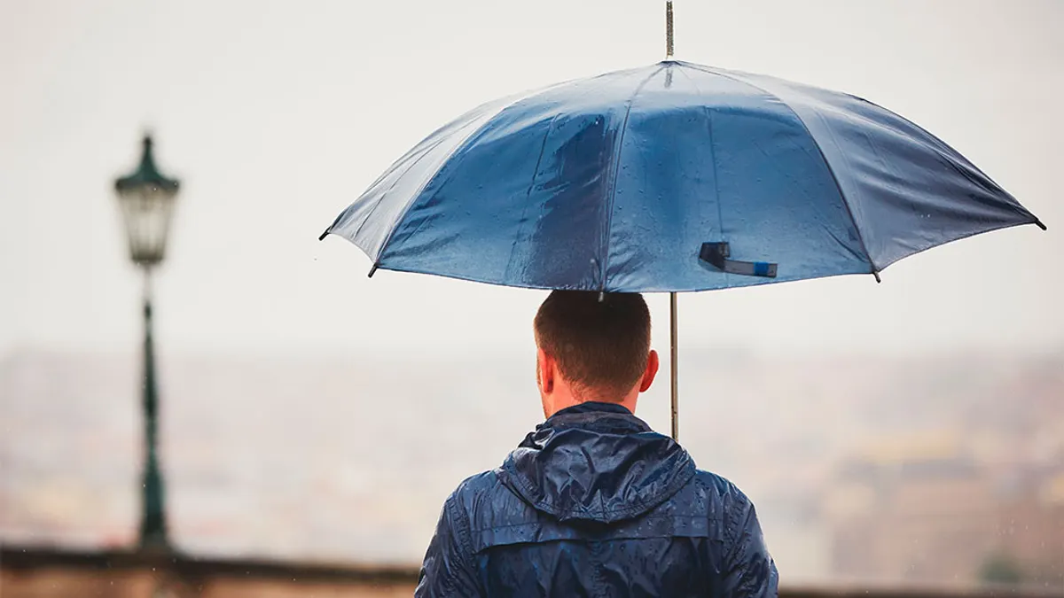Rainy day. Young man is holding blue umbrella and walking in rain.