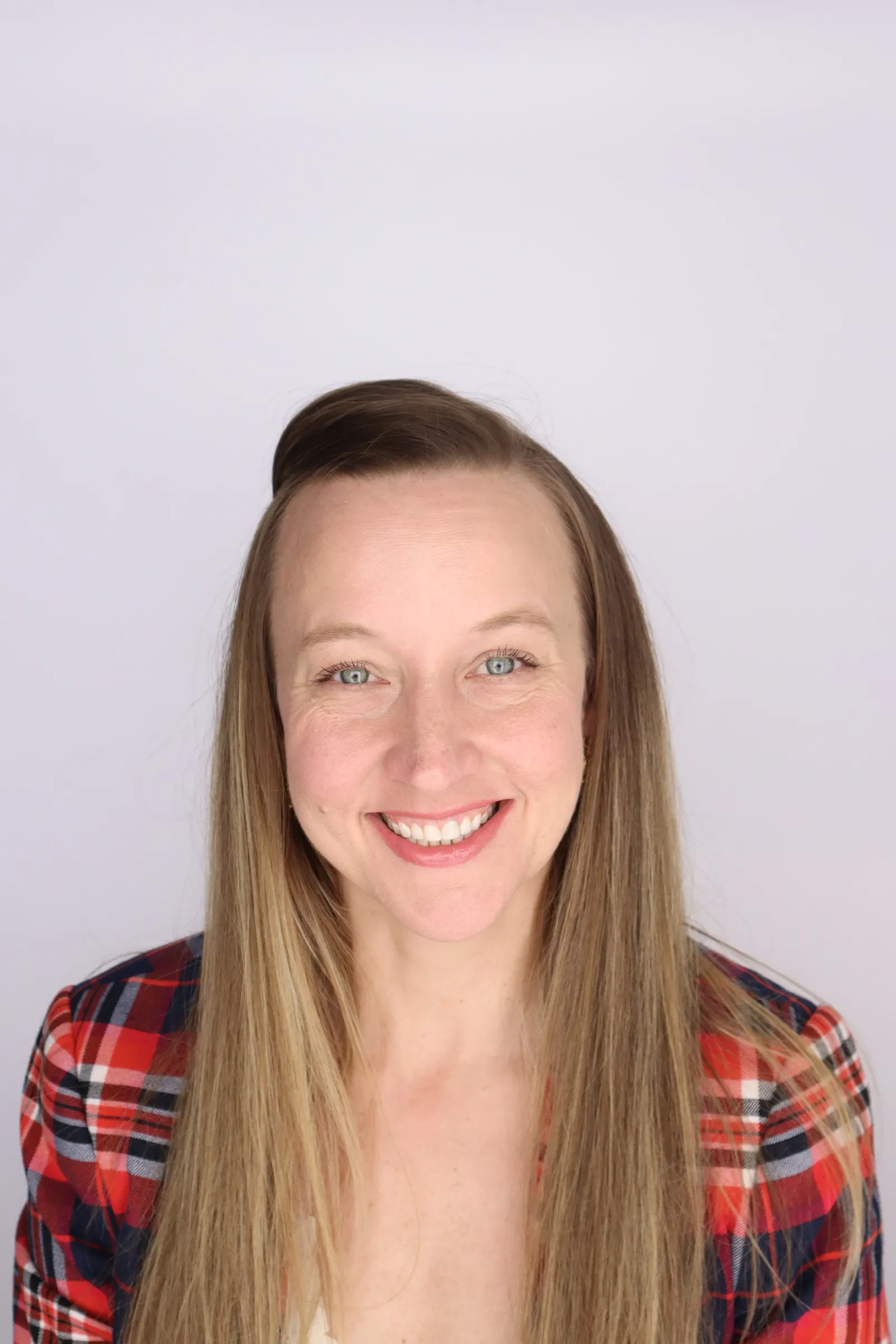 A person wearing a plaid jacket smiles for the camera in front of a light-colored background.