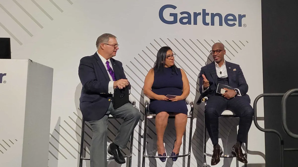 Three speakers on a conference stage with Gartner signage in the background