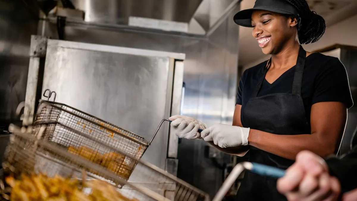 A woman in a black apron serves fries to customers in a bustling restaurant setting.