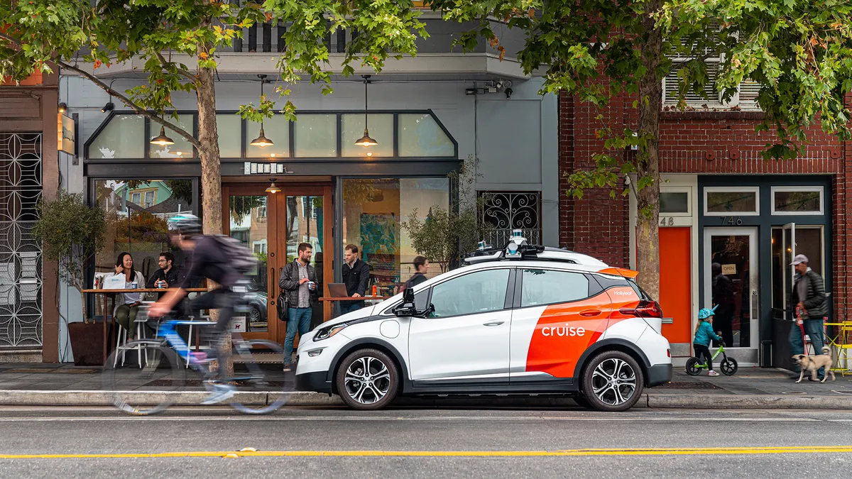 A white and orange painted Chevy Bolt EV operated by Cruise parked in front of a cafe in the Hayes Valley neighborhood of San Francisco.