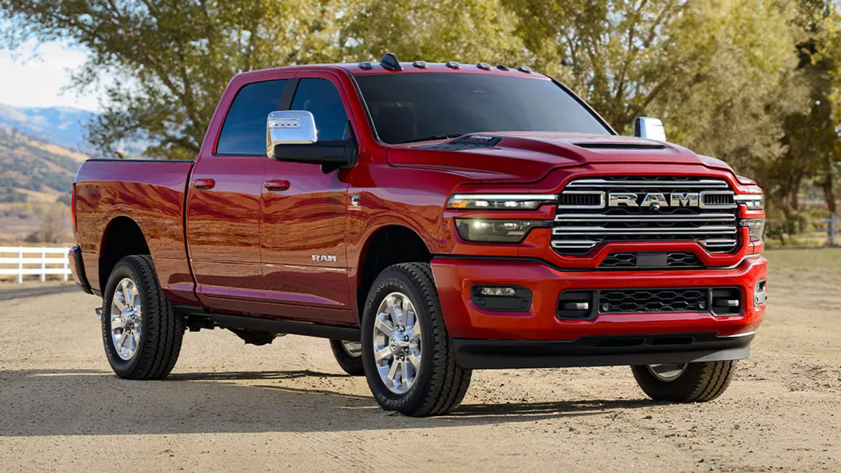 A red 2025 Ram 2500 pickup parked outdoors with a white fence in the background.