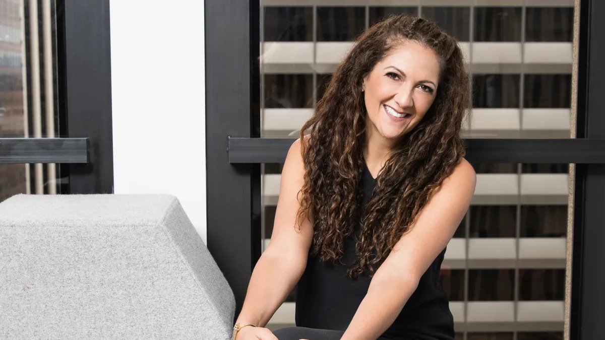 Sephora executive Artemis Patrick poses for a sitting headshot in black pants, a black blouse and red shoes.