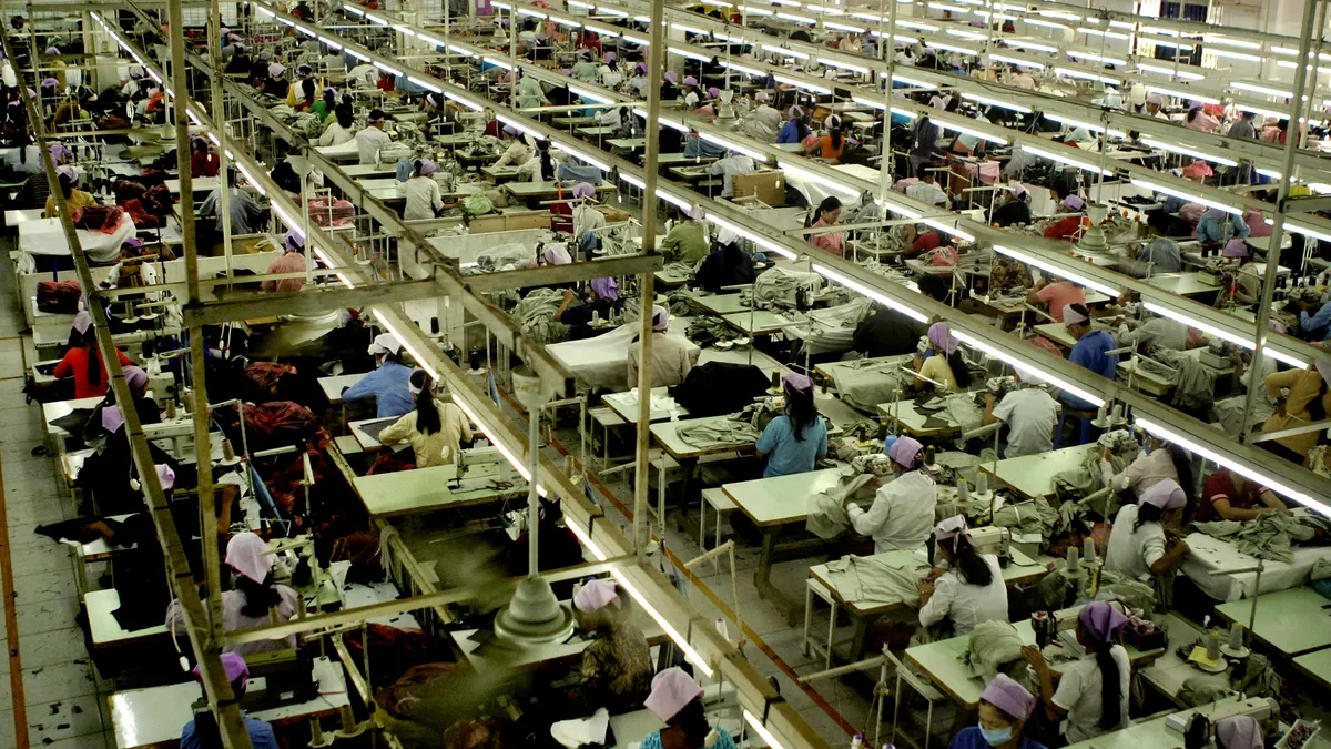 An overhead view of a garment factory floor shows workers using sewing machines.