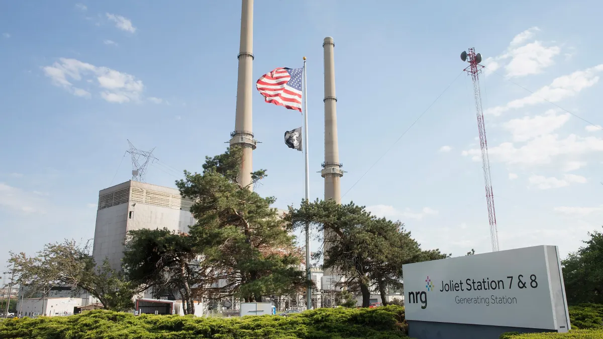 A power plant seen against a blue sky with an American flag in front and a sign that says "Joliet Station 7&8 Generating Station"