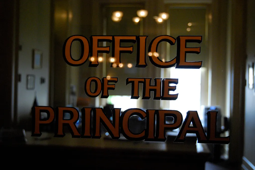 The door to a principal's office is shown. "Office of the Principal" is painted on the door's window.