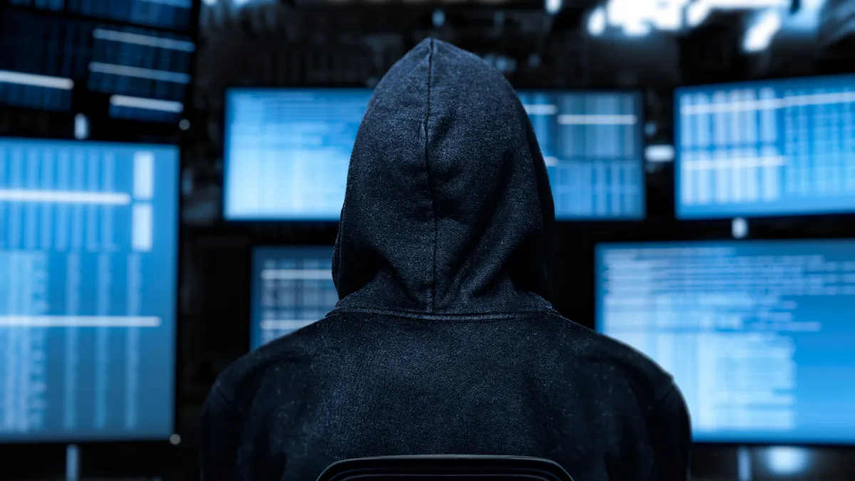 Image of a hacker facing a computer screen with blue text