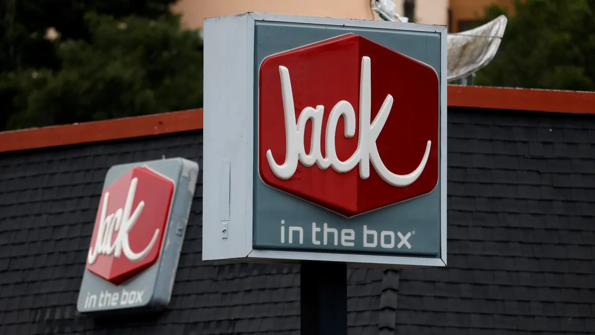 A photograph of a gray sign with a red box inside with white letters that says "Jack" under the box it says "in the box."