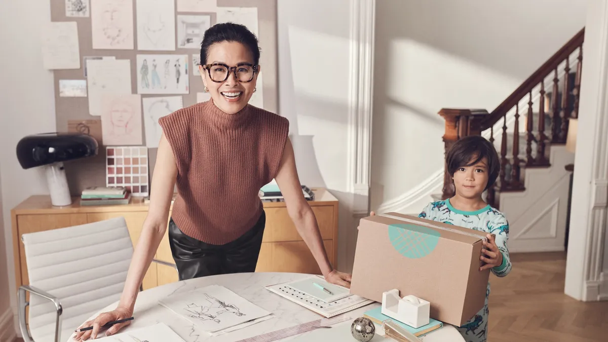 A person wearing glasses leans over a table with sketches as a child looks on.