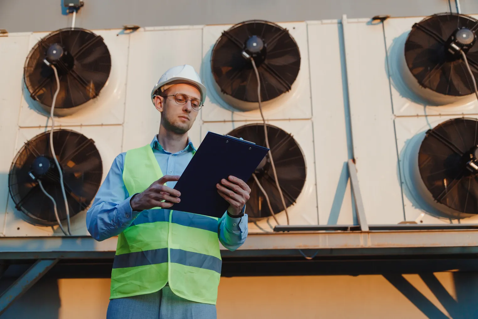 A technician looks at a work order form in front of a industrial HVAC units.