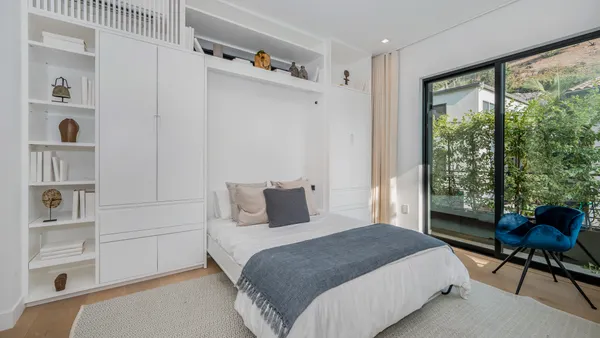 A bedroom with a wall bed, chair and shelves above the bed.