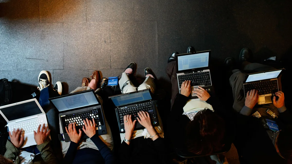 An overhead view of people sitting with laptops on their laps using their hands to type.