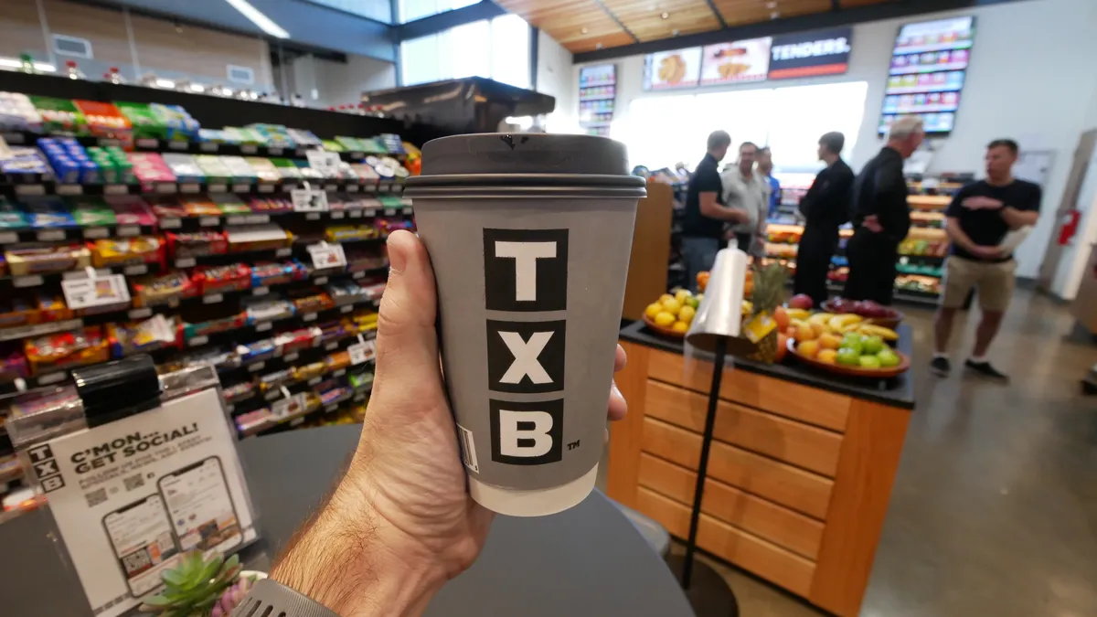 A photo of a hand holding a cup of coffee from TXB, inside the store.