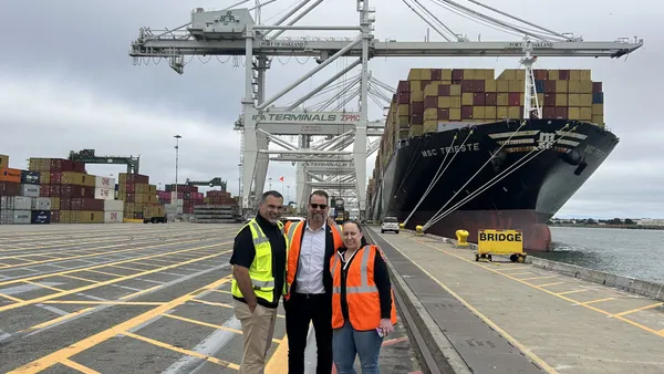 Three people posing in front of a container vessel at the Port of Oakland.