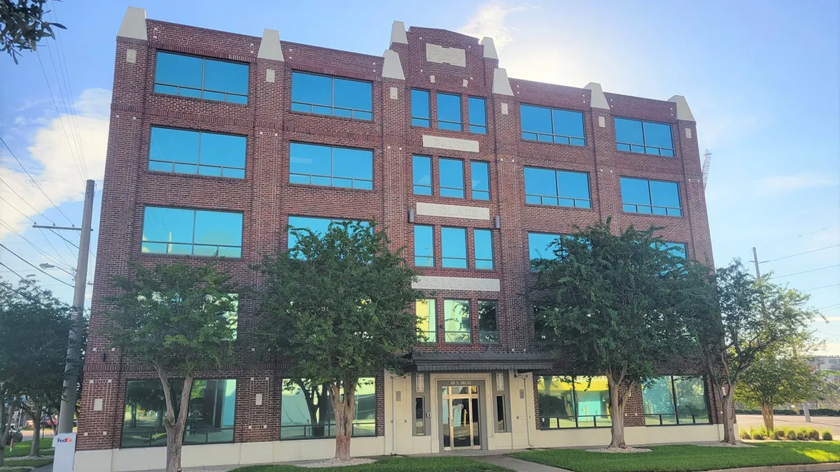 A large, seemingly brick building looms in the foreground. A blue sky at midday is in the background.