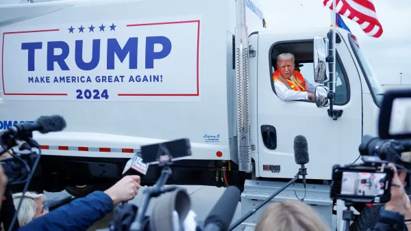 Former President Donald Trump sits in the cab of a garbage truck emblazoned with his campaign's logo as reporters look on.