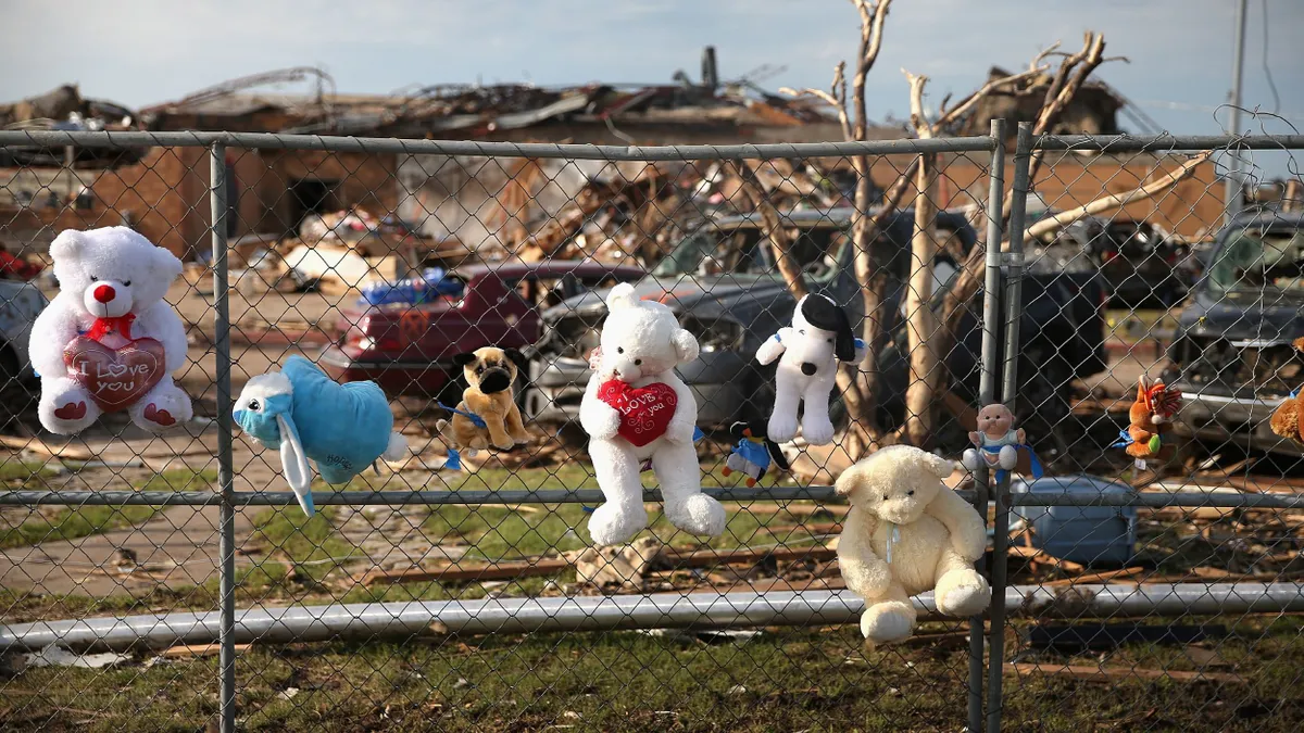 A row of stuffed animals are attached to a fence in front of the rubble left behind from a lethal tornado that hit an elementary school on May 20, 2013.