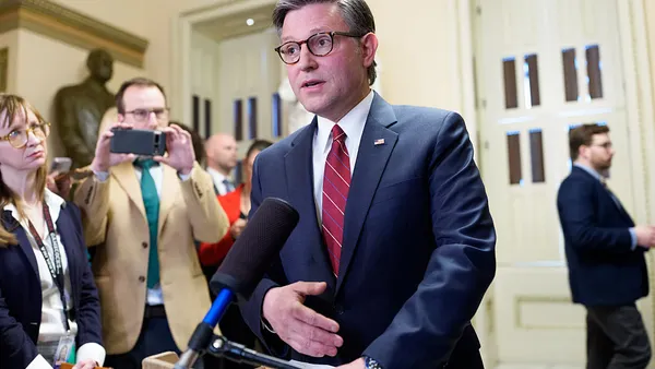 A person stands in front of a microphone while other people ate standing around him.