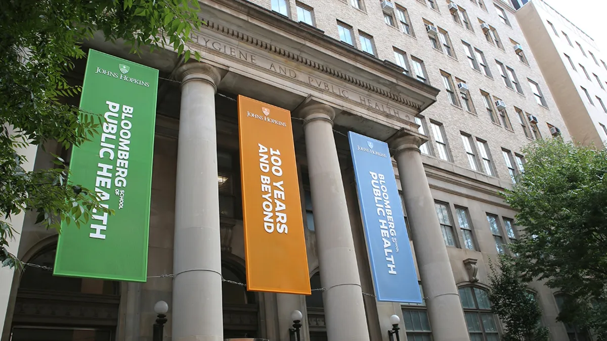 The front of an academic building with coliseum pillars. Between the pillars are hanging banners in orange, green and blue.