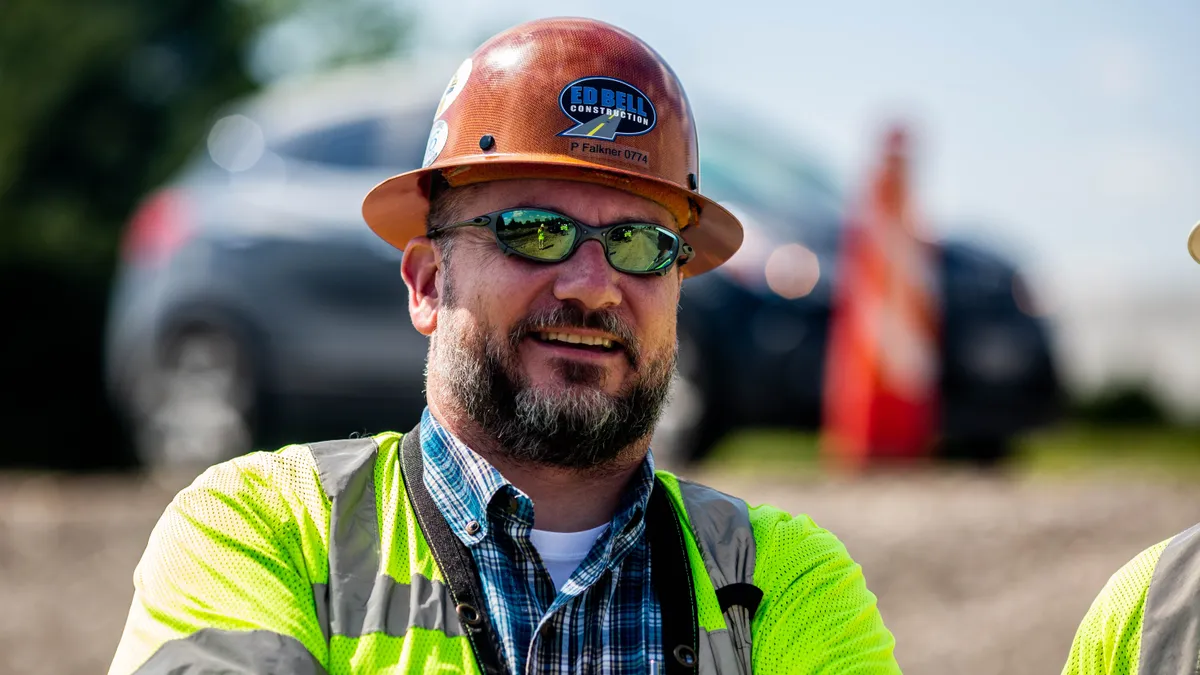 A headshot of Phillippe Falkner of Ed Bell Construction in a jobsite. He wears a hard hat, safety vest and sunglasses.