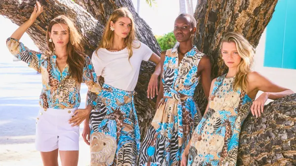 Four models stand outside, against a large tree, each wearing Lilly Pulitzer clothing that includes animal print.