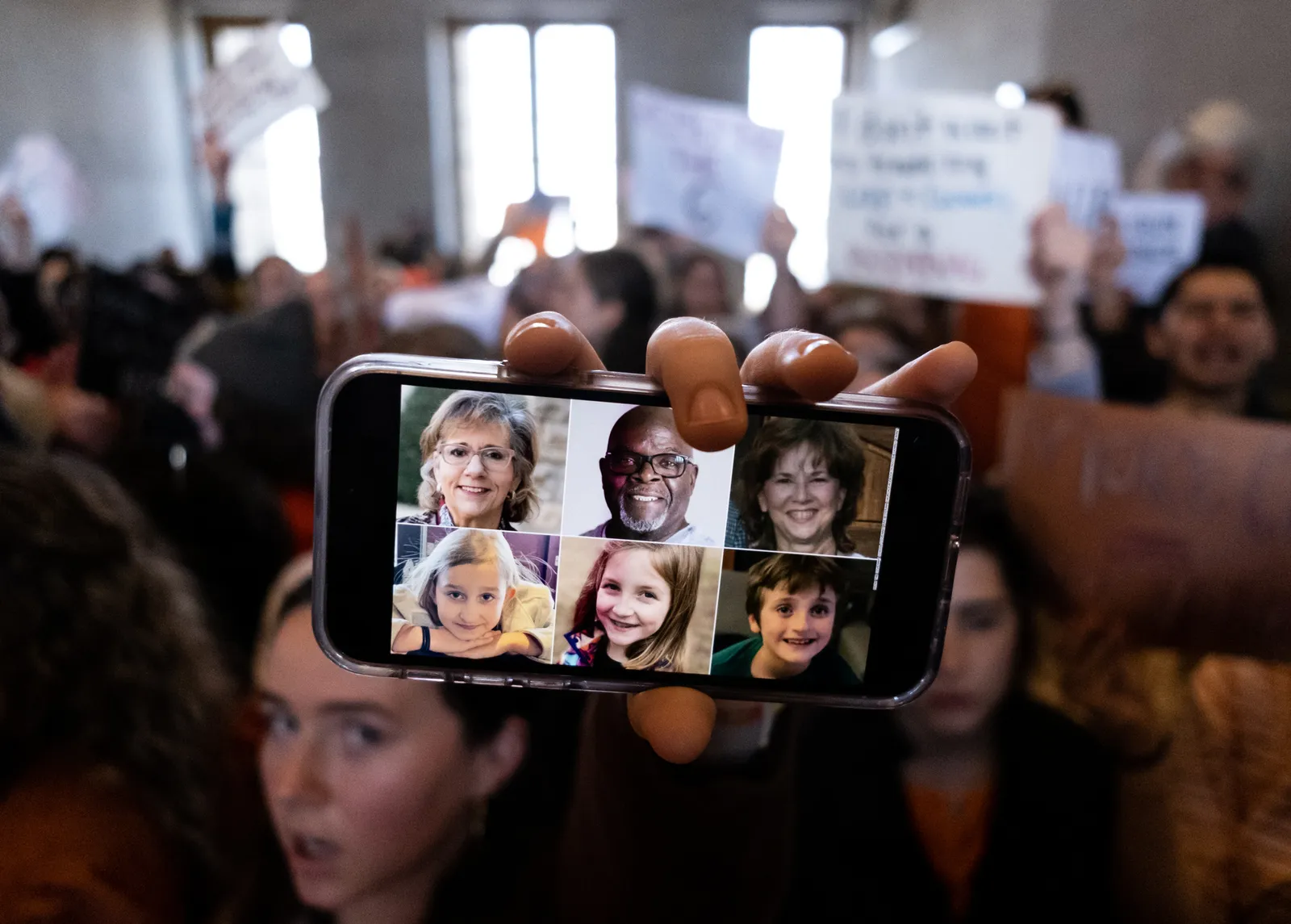 A photo of victims is displayed on a phone screen at a protest