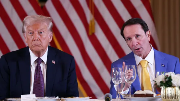 President Trump and Louisiana Gov. Jeff Landry sit at a table with a white tablecloth and two empty wine glasses with American flag behind them.