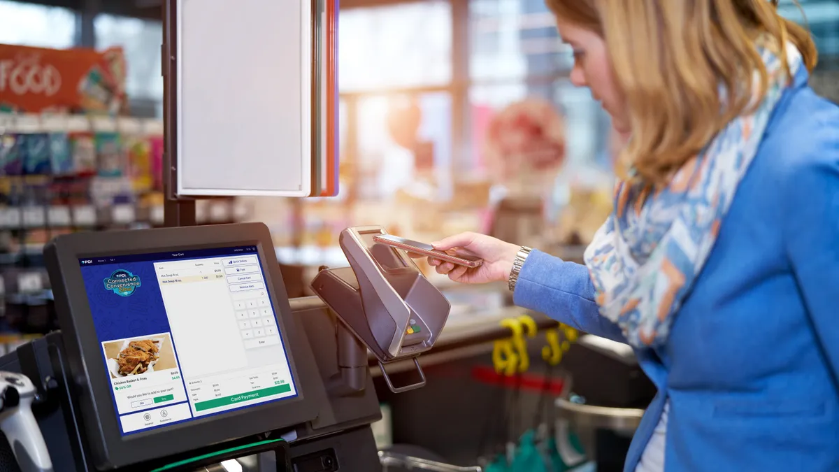 A photo of a person using their phone to pay for purchases at a self-checkout kiosk.