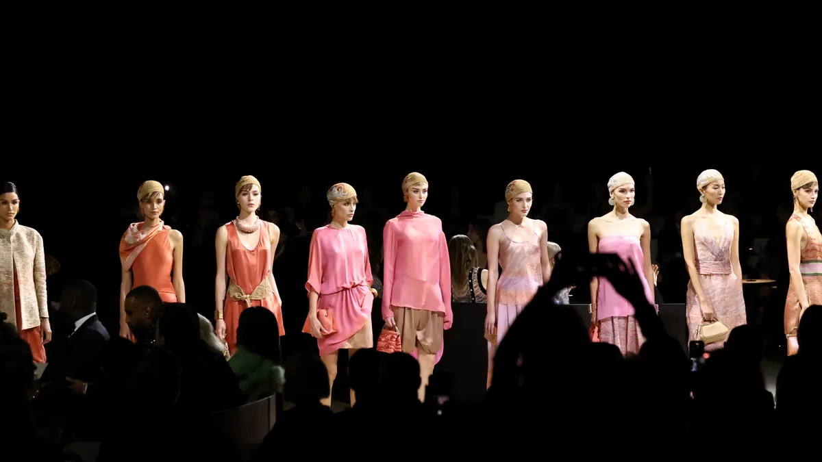 Models in pastel outfits stand in a line on a dark runway.