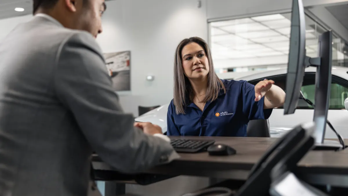Person wearing a vAuto polo and looking at a computer with another person in a suit.