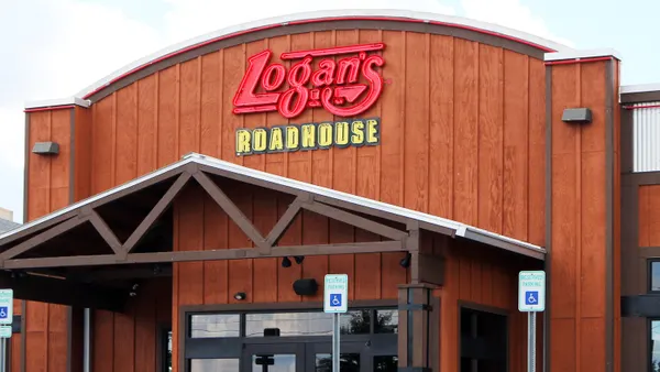 An image ofa brown building with wood paneling. There is a parking lot out front. It has a logo with Logan's in red and Roadhouse in yellow underneath