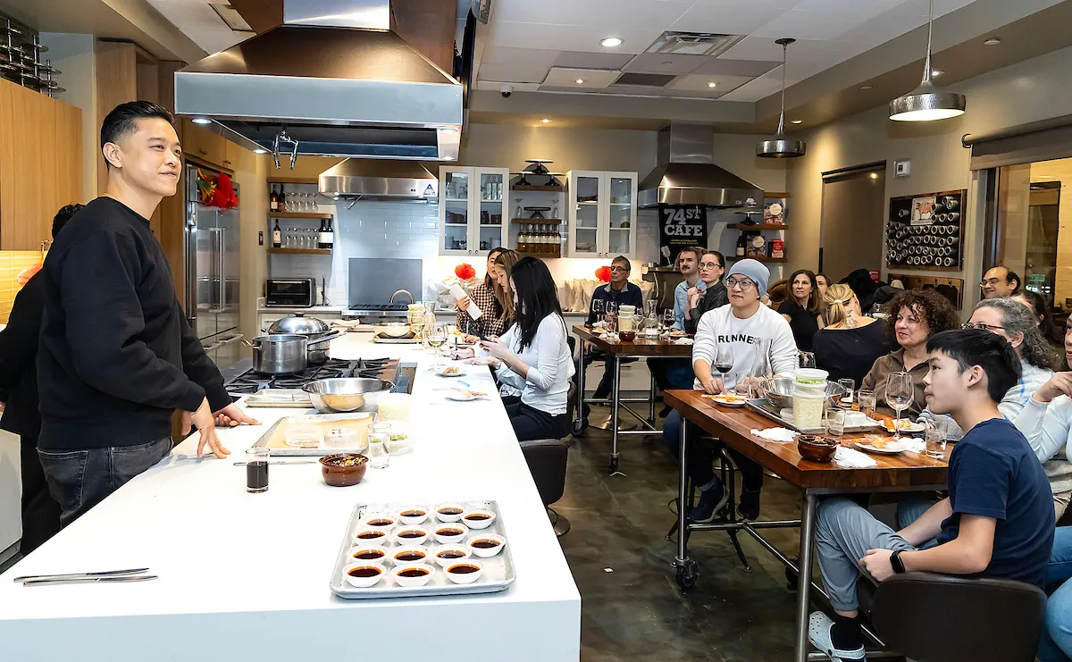 A person standing at a counter with food on it in front of people sitting around tables.
