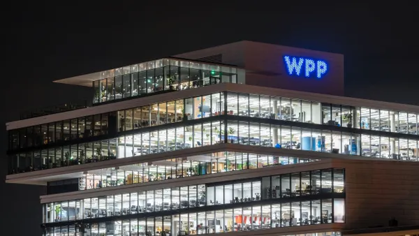 A tiered office building with large glass windows, brightly lit from within at night; the top of the building reads "WPP" in blue lights.